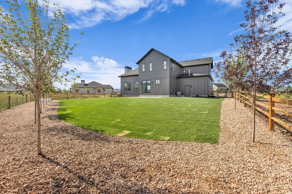 Expansive rear yard featuring a manicured lawn, established trees, and a wooden split-rail fence