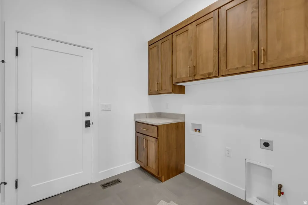 Laundry area featuring wood-finish cabinetry, a light-toned countertop, and modern gray flooring