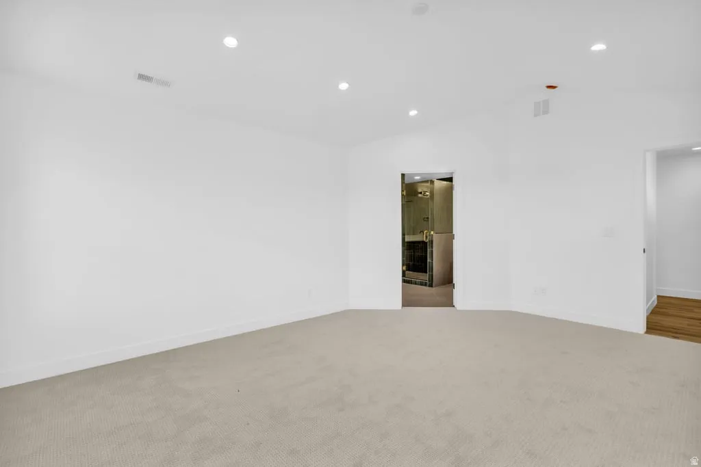 Spacious room featuring vaulted ceilings, recessed lighting, neutral carpeting, and white baseboards