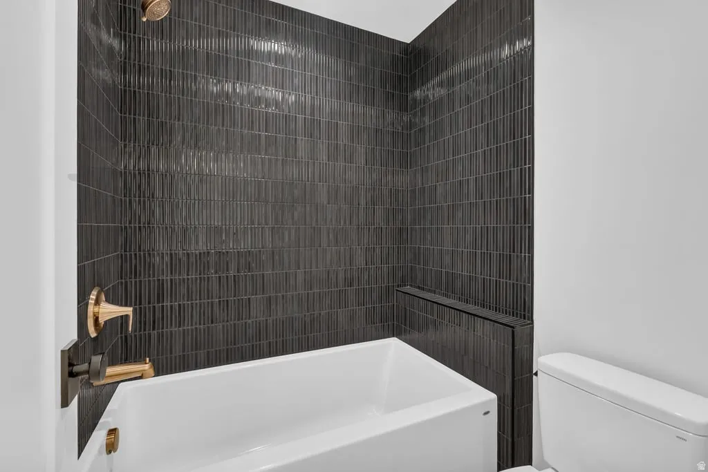 Bathtub with textured dark tile surround, integrated tiled shelf, and brass-finish fixtures