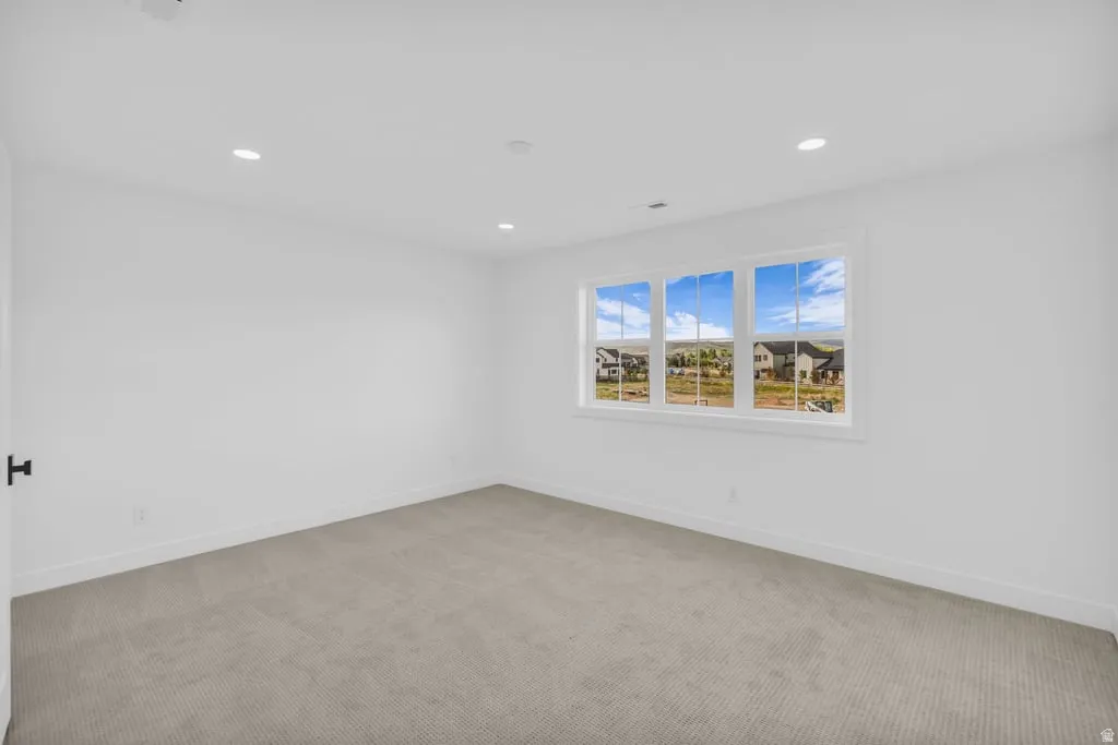 Bright room featuring crisp white walls, recessed lighting, a triple window, and neutral carpeting