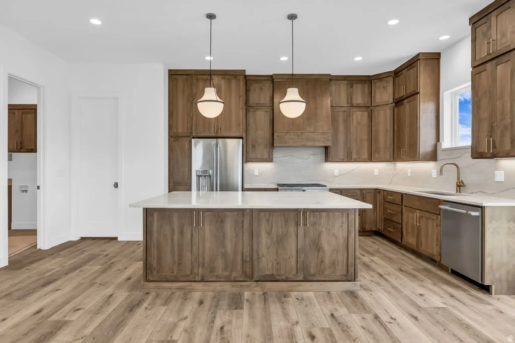 Spacious kitchen featuring an expansive center island, wood-finish flooring, stainless steel appliances, and abundant cabinetry