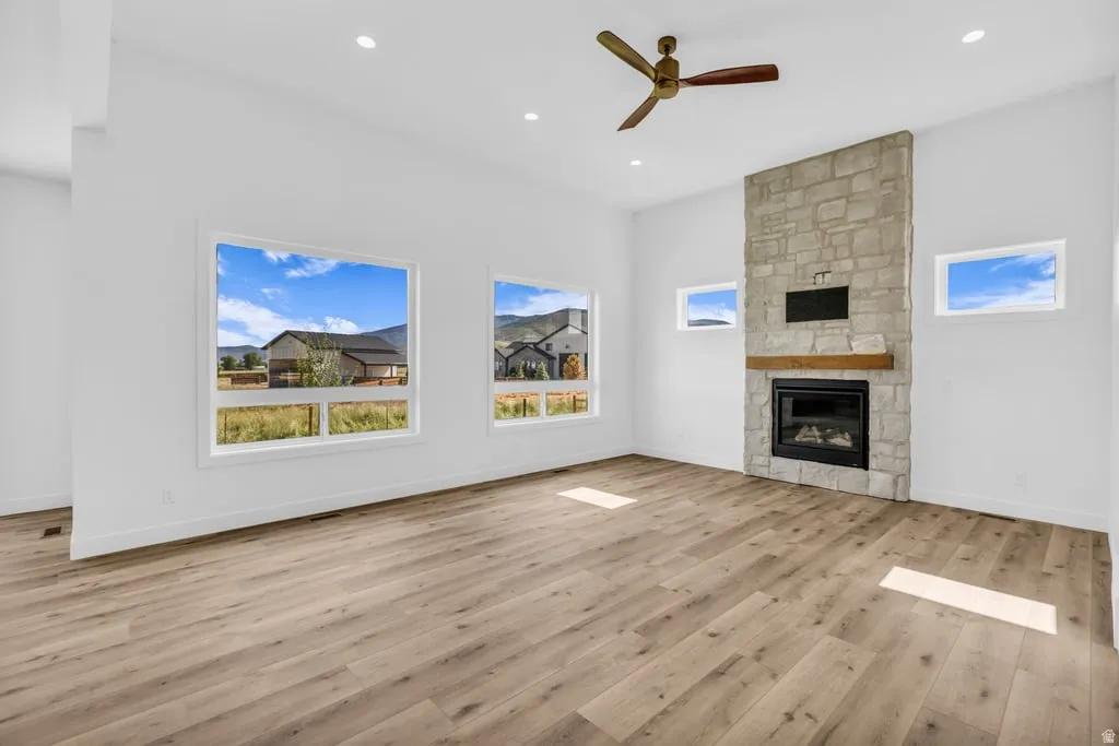 Spacious room featuring wood-finish flooring, a stone fireplace with a wood mantle, and a ceiling fan