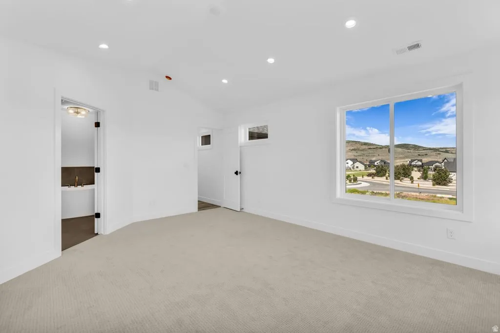 Spacious room featuring light-colored carpeting, recessed lighting, and a large window offering expansive mountain and neighborhood scenery