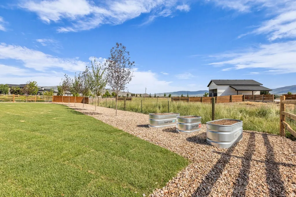 Expansive grassy area featuring a gravel pathway, three galvanized metal planters, and a wooden perimeter fence