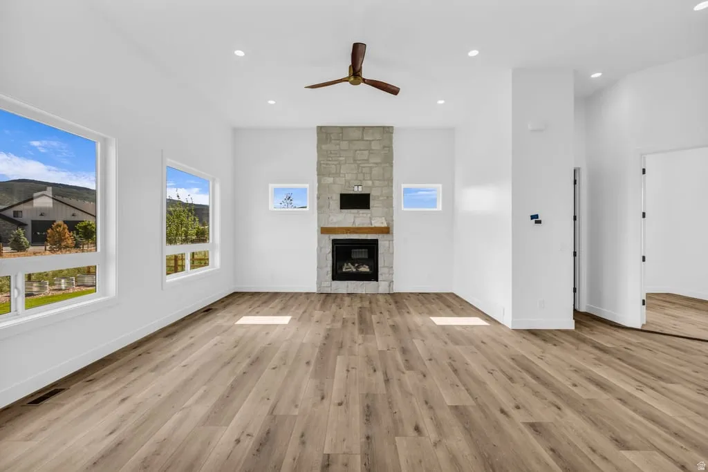 Spacious living area featuring a floor-to-ceiling stone fireplace, wood-finish flooring, a ceiling fan, and recessed lighting