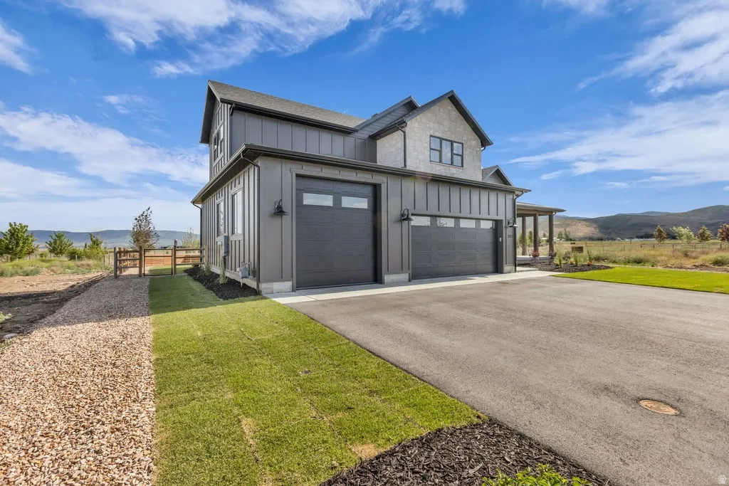 Modern farmhouse exterior featuring board and batten siding, a two-car garage with contemporary doors, an expansive asphalt driveway, and a covered front porch