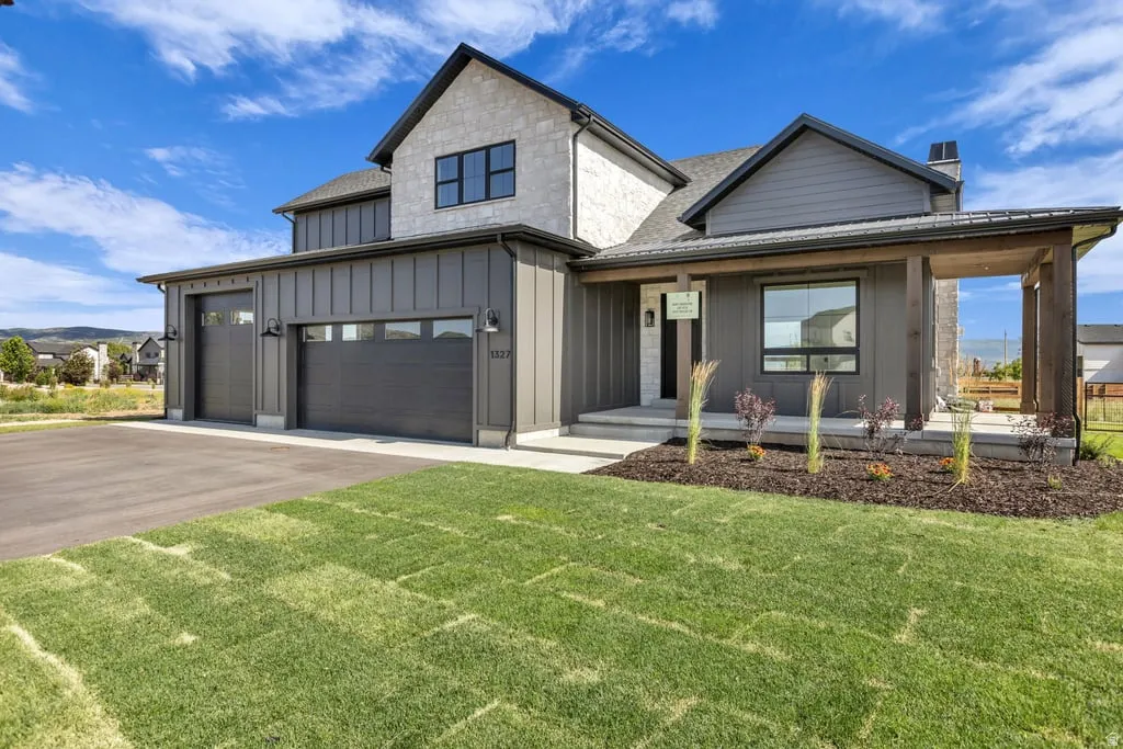 Modern farmhouse exterior featuring board and batten siding, stone accents, a covered entry porch with wood-finish columns, a two-car garage with transom windows, and a landscaped front yard