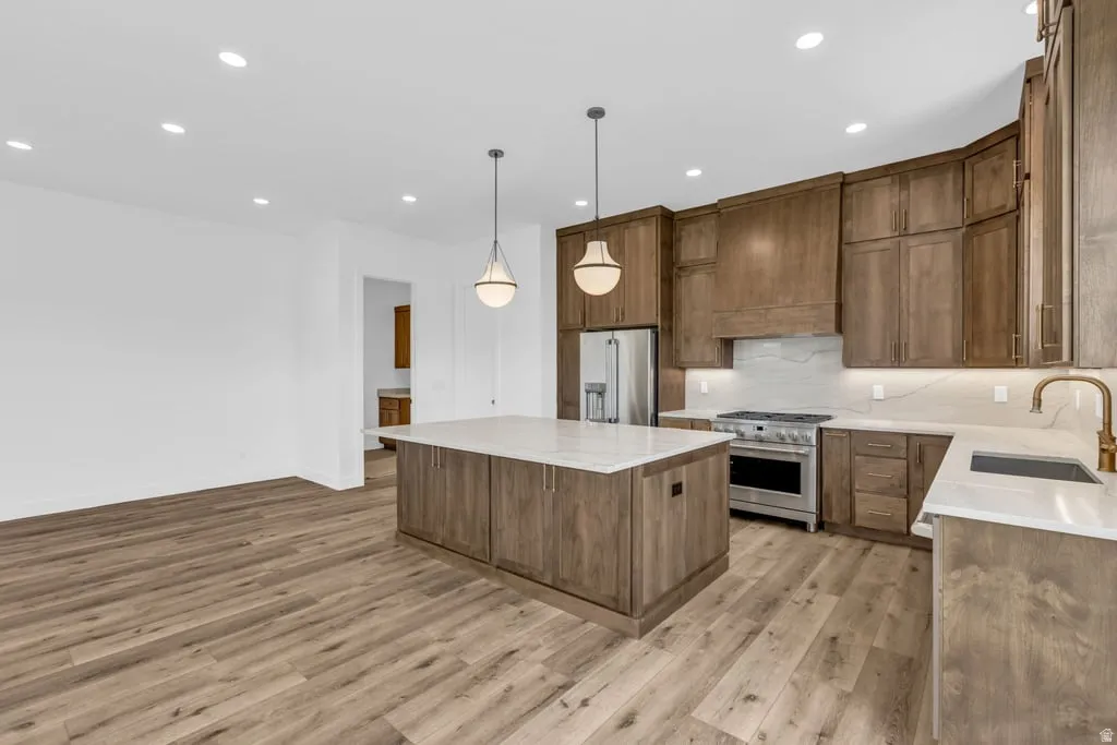 Spacious kitchen featuring wood-finish flooring, a large island with pendant lighting, stainless steel appliances, and extensive wood cabinetry with light countertops and backsplash