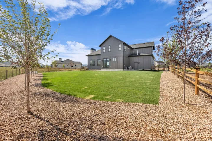Expansive rear yard featuring a manicured lawn, established trees, and a wooden split-rail fence