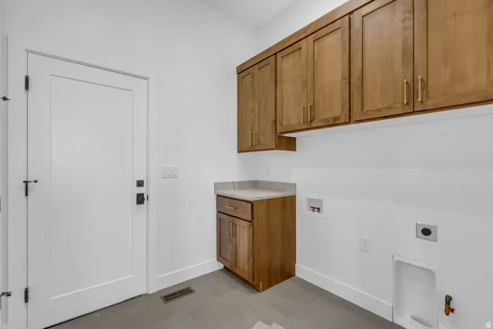 Laundry area featuring wood-finish cabinetry, a light-toned countertop, and modern gray flooring