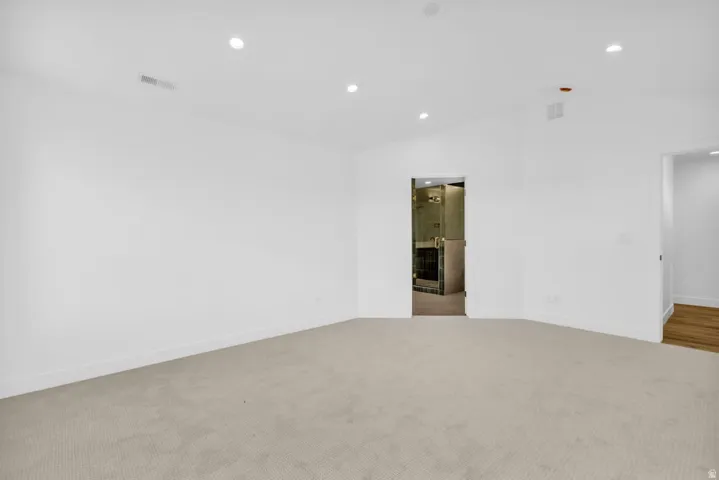Spacious room featuring vaulted ceilings, recessed lighting, neutral carpeting, and white baseboards