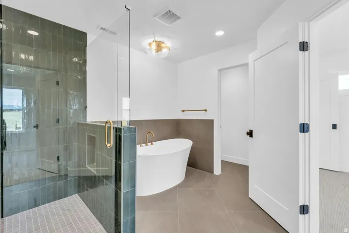 Spacious bathroom featuring a glass-enclosed shower with vertical tile, a freestanding soaking tub, and large format floor tiling