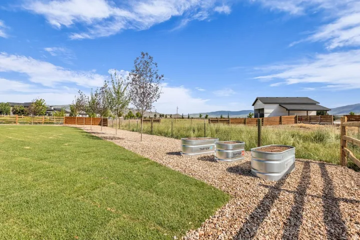 Expansive grassy area featuring a gravel pathway, three galvanized metal planters, and a wooden perimeter fence