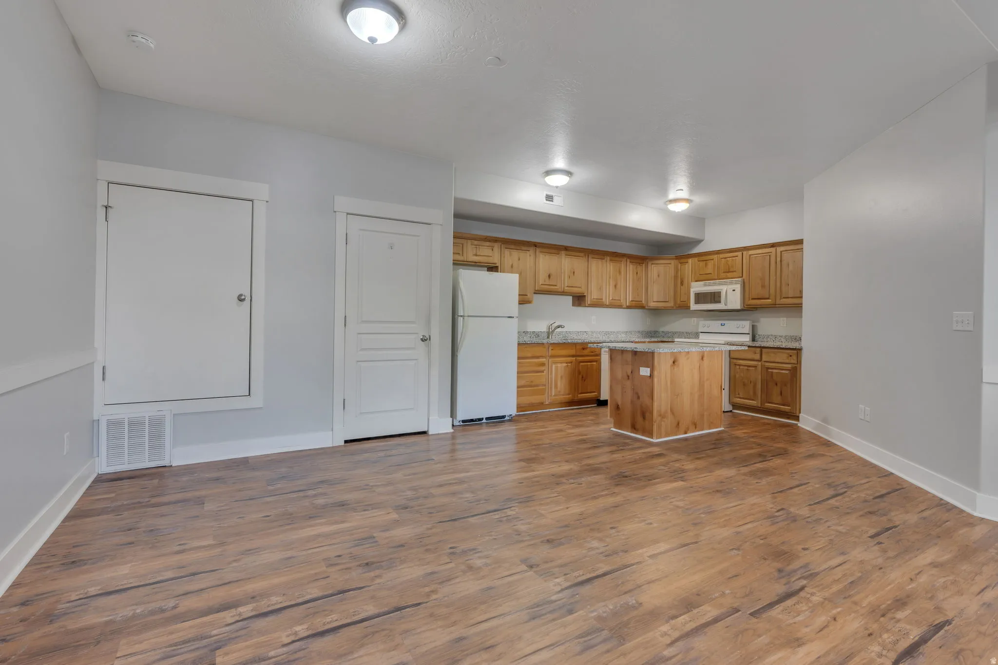 Open-concept living space featuring wood-finish flooring, recessed lighting, and a kitchen with wood cabinetry, light-toned countertops, and a central island