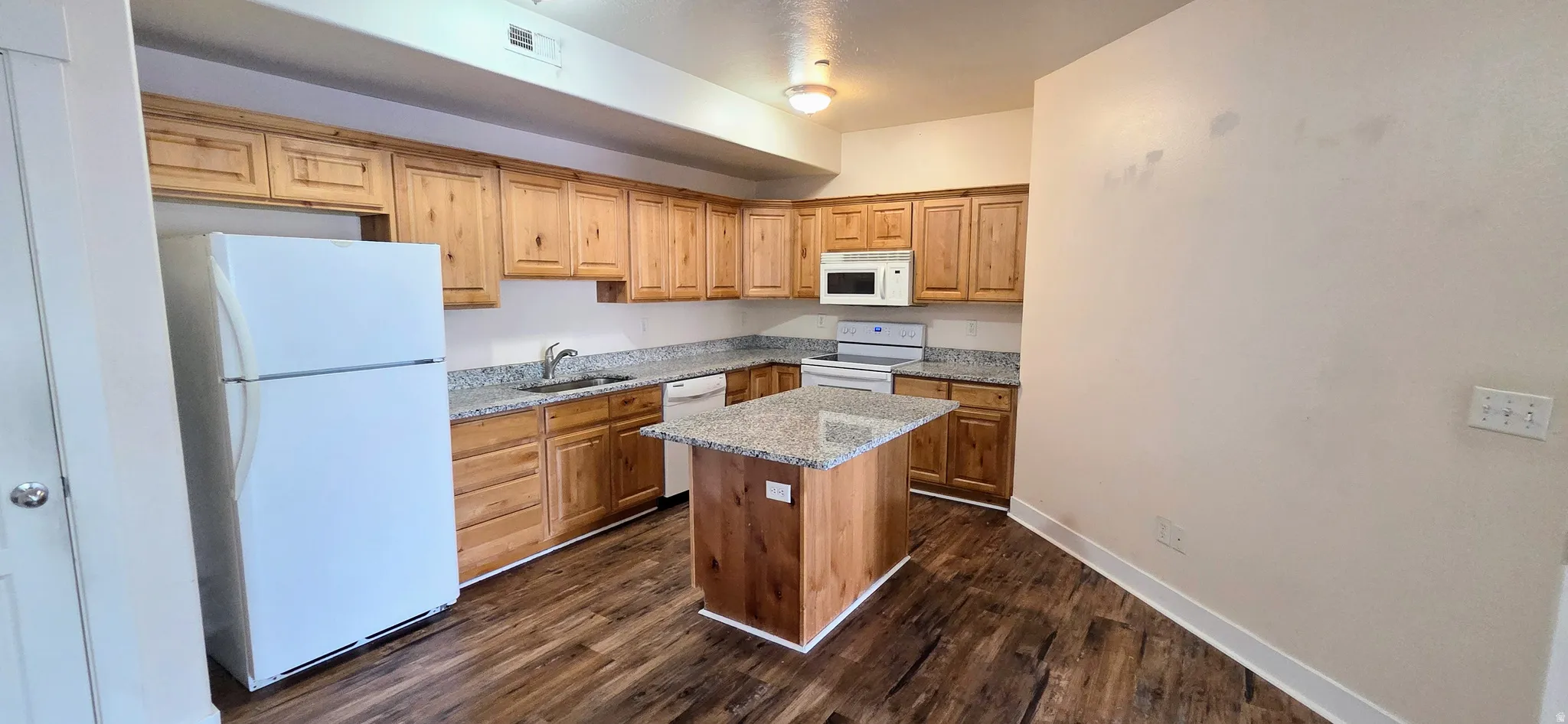 Kitchen featuring wood-finish flooring, a central island with a stone-finish countertop, light wood cabinetry, and white appliances including a refrigerator, microwave, and range