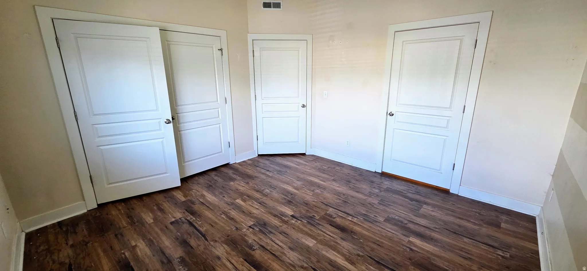Interior room featuring wood-finish flooring, white trim, and multiple white paneled doors with silver hardware