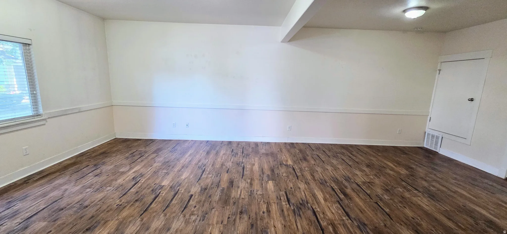 Spacious room featuring wood-finish flooring, white walls with wainscoting, and a window with blinds