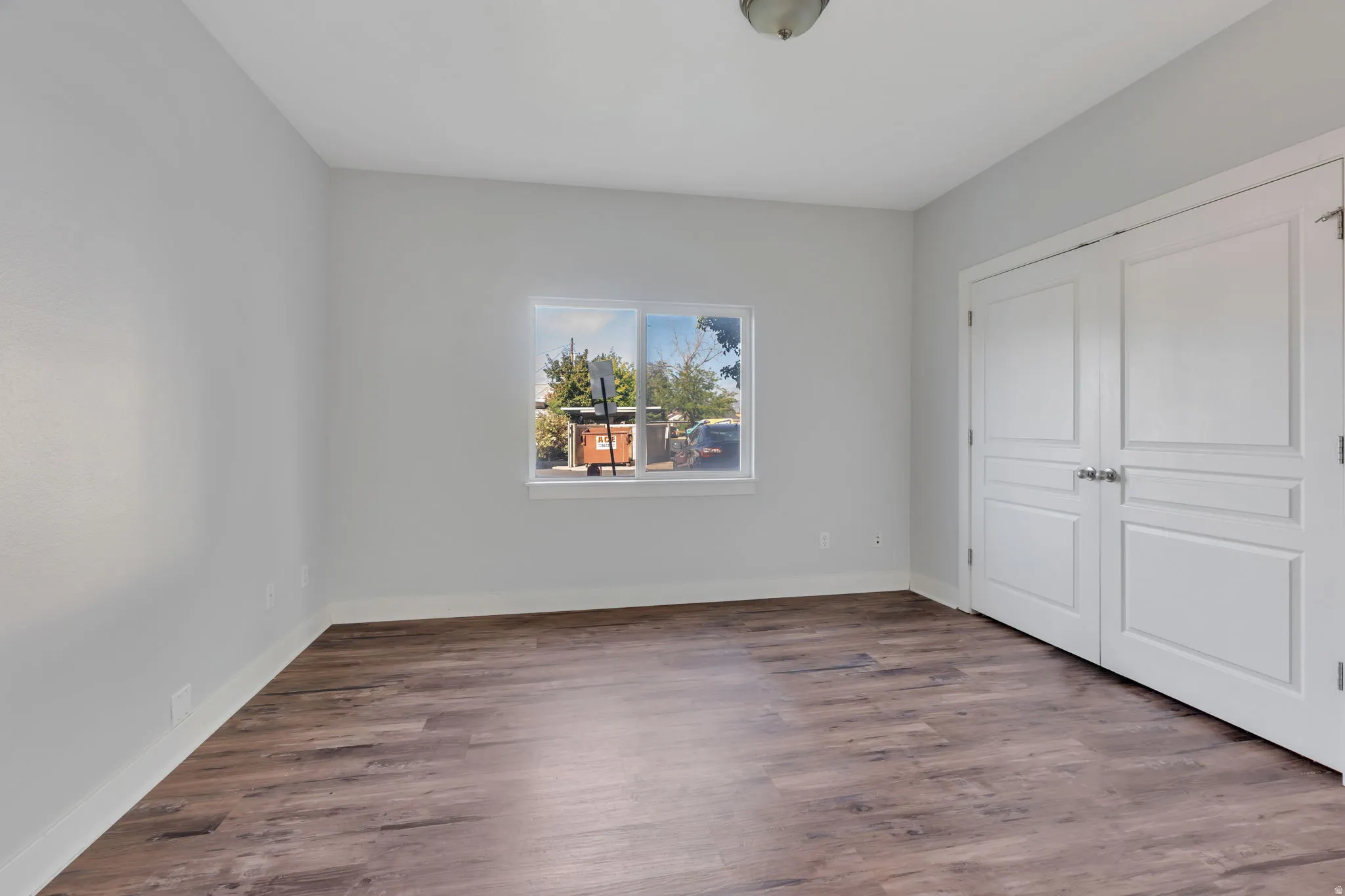 Wood-finish flooring, white trim, a single window, and a white ceiling light fixture