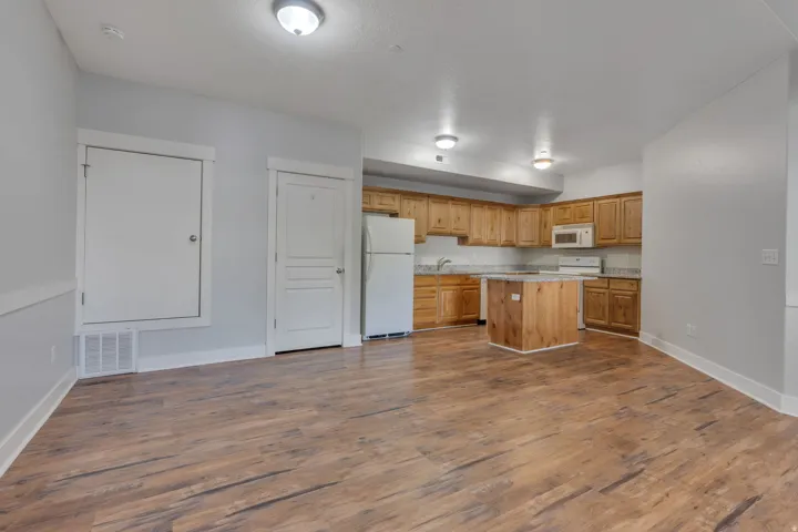 Open-concept living space featuring wood-finish flooring, recessed lighting, and a kitchen with wood cabinetry, light-toned countertops, and a central island