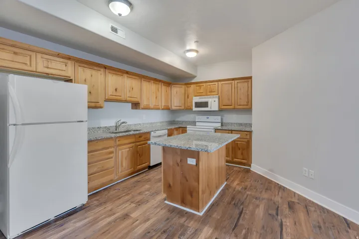 Kitchen featuring wood-finish flooring, wood cabinetry, granite-style countertops, an island with a granite-style top, and white appliances