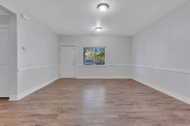 Spacious room featuring wood-finish flooring, neutral paint, a paneled door, and a window with white trim