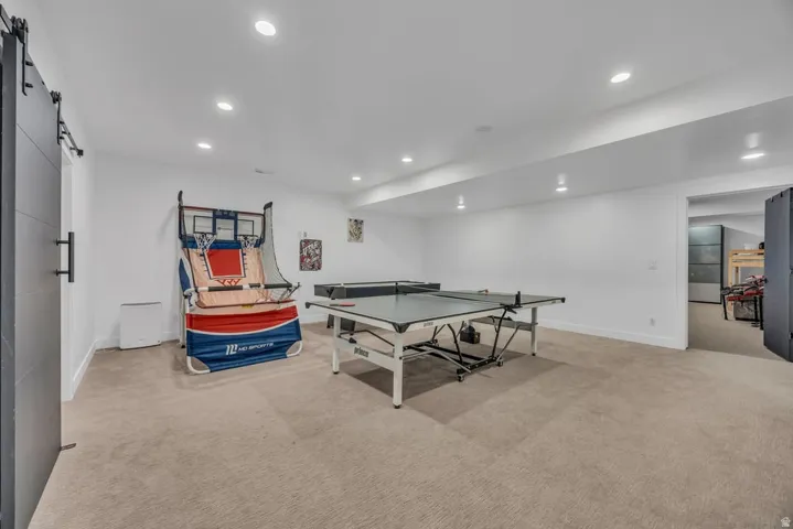 Spacious room featuring neutral carpet flooring, recessed lighting, white walls, and a modern barn door with black hardware