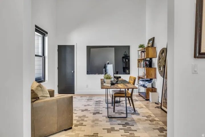 Open-concept room featuring wood-finish flooring, a contemporary black door, and a tall window with roller shade