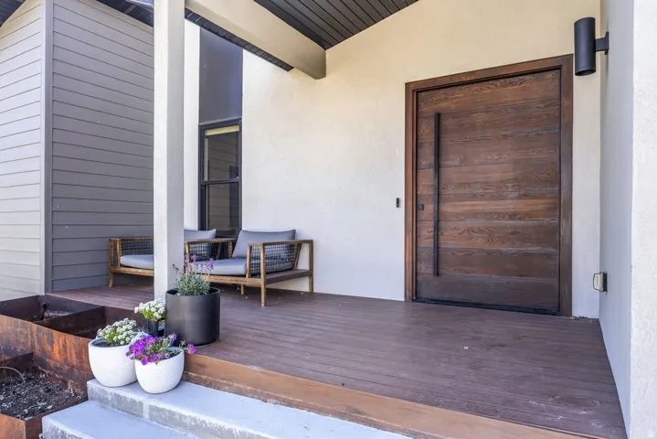 Inviting porch entry featuring a contemporary wood-finish door with a long black pull handle, durable composite decking, and a textured stucco exterior
