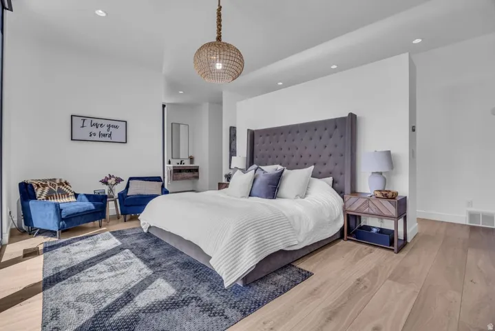 Spacious room featuring light wood-finish flooring, recessed lighting, a decorative hanging fixture, and a partial wall element