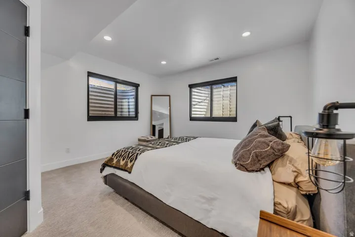 Bedroom featuring two windows with black trim, recessed ceiling lighting, and light-toned carpeting