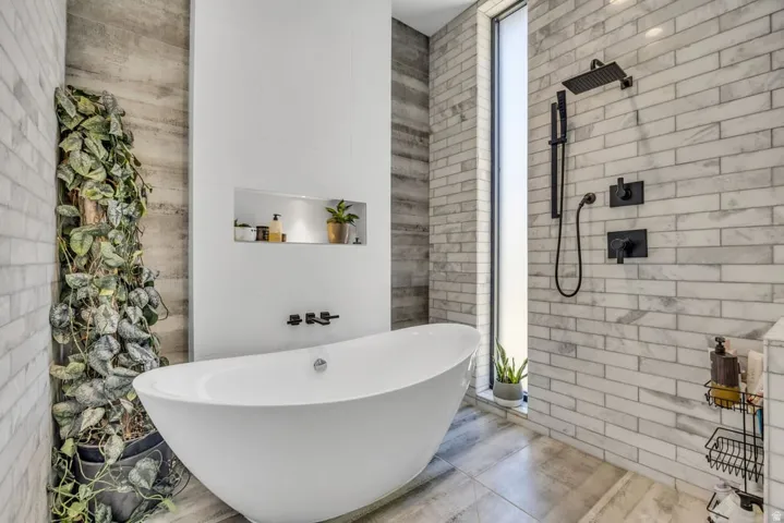 Modern bathroom featuring a freestanding soaking tub, matte black fixtures, a vertical window, a built-in recessed shelf, and subway-style wall tiling