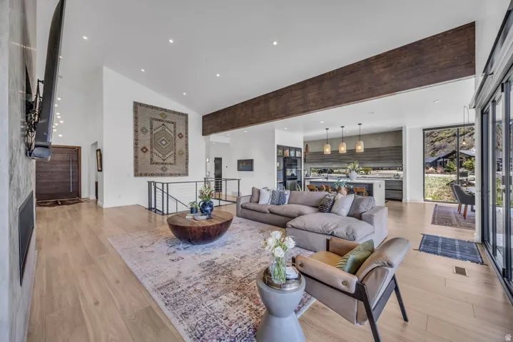 Open-concept living area with vaulted ceilings, light wood-finish flooring, and a prominent wood beam detail