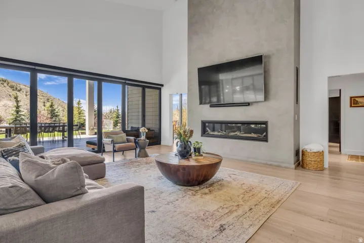 Spacious living area featuring high ceilings, a full-height textured accent wall with an integrated linear fireplace, and light wood-finish flooring