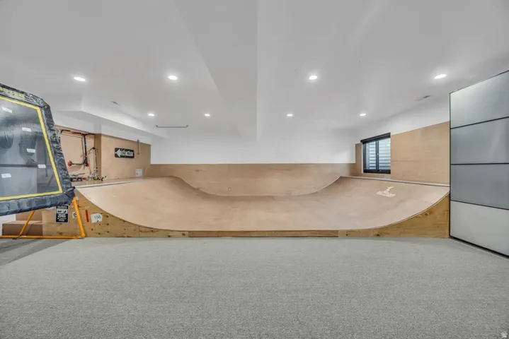 Recreational room featuring a built-in skateboard ramp, wood-finish wall paneling, recessed lighting, and grey carpeting
