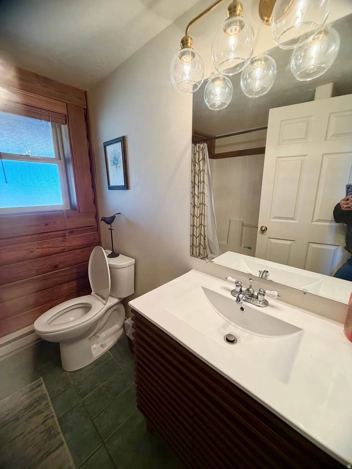 Modern vanity with integrated sink, wood-finish slatted cabinetry, and an overhead multi-bulb light fixture