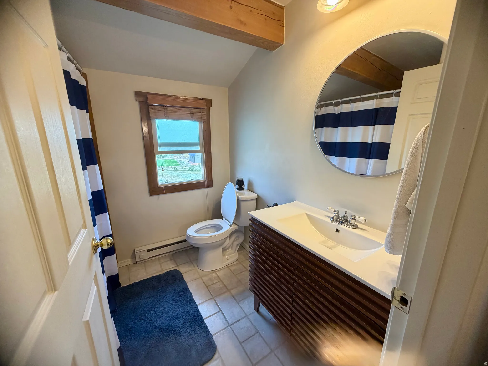 Bathroom featuring a wood-finish vanity with an integrated sink, a circular wall mirror, and exposed ceiling beams