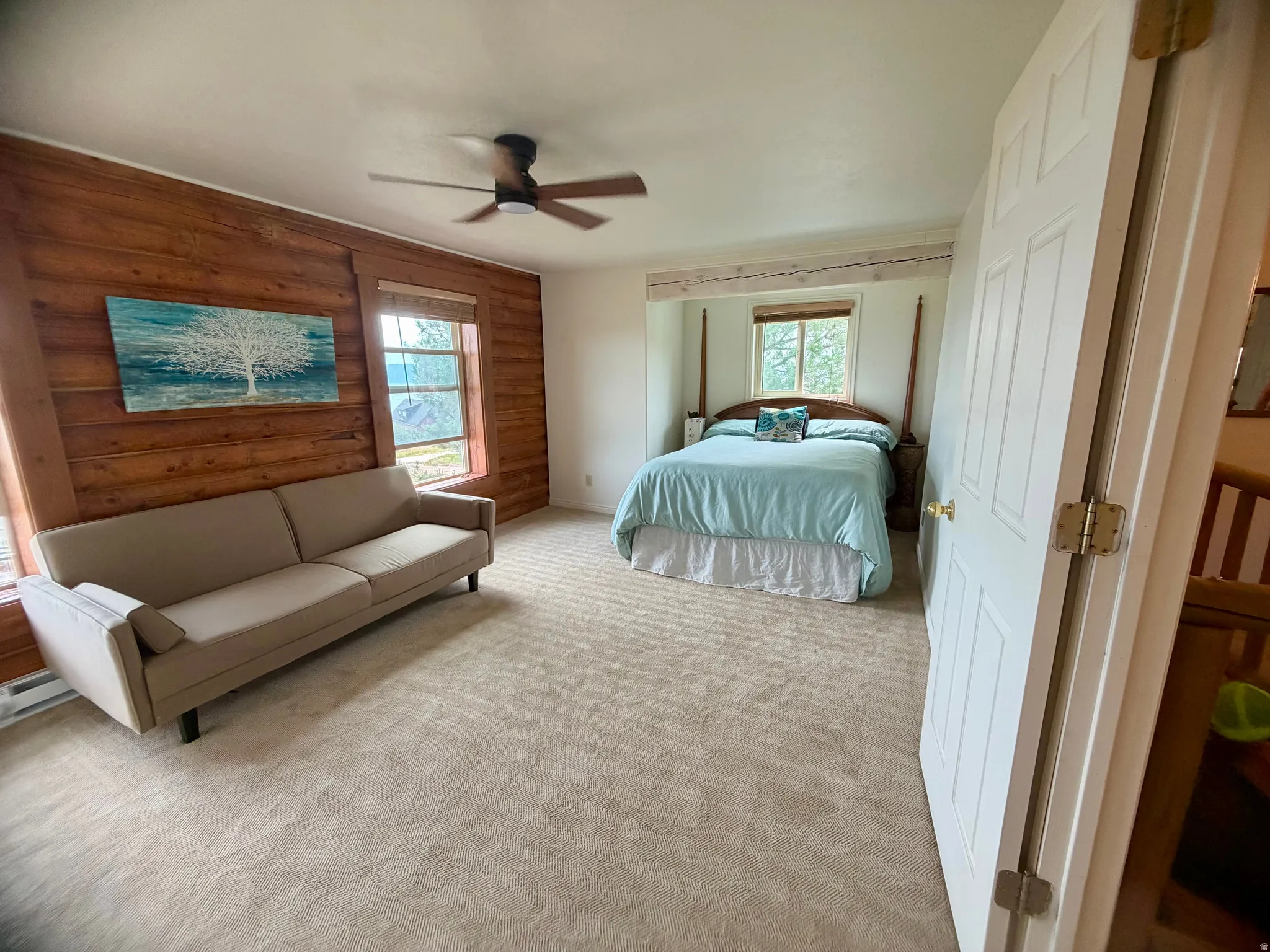 Carpeted room featuring a ceiling fan, a wood-paneled accent wall, and two windows with natural light