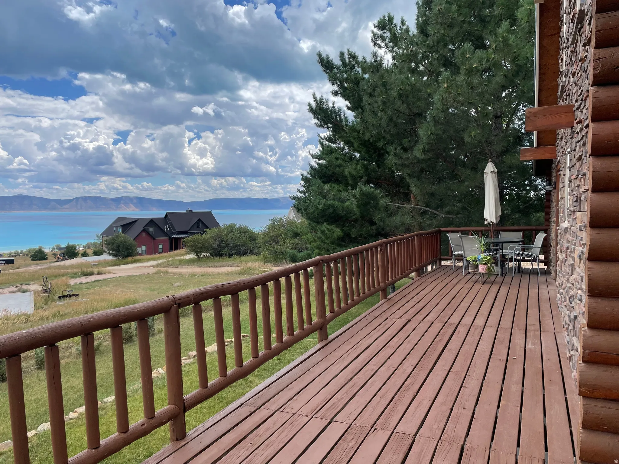 Expansive wood deck with a log railing, stone and log exterior, and mature trees