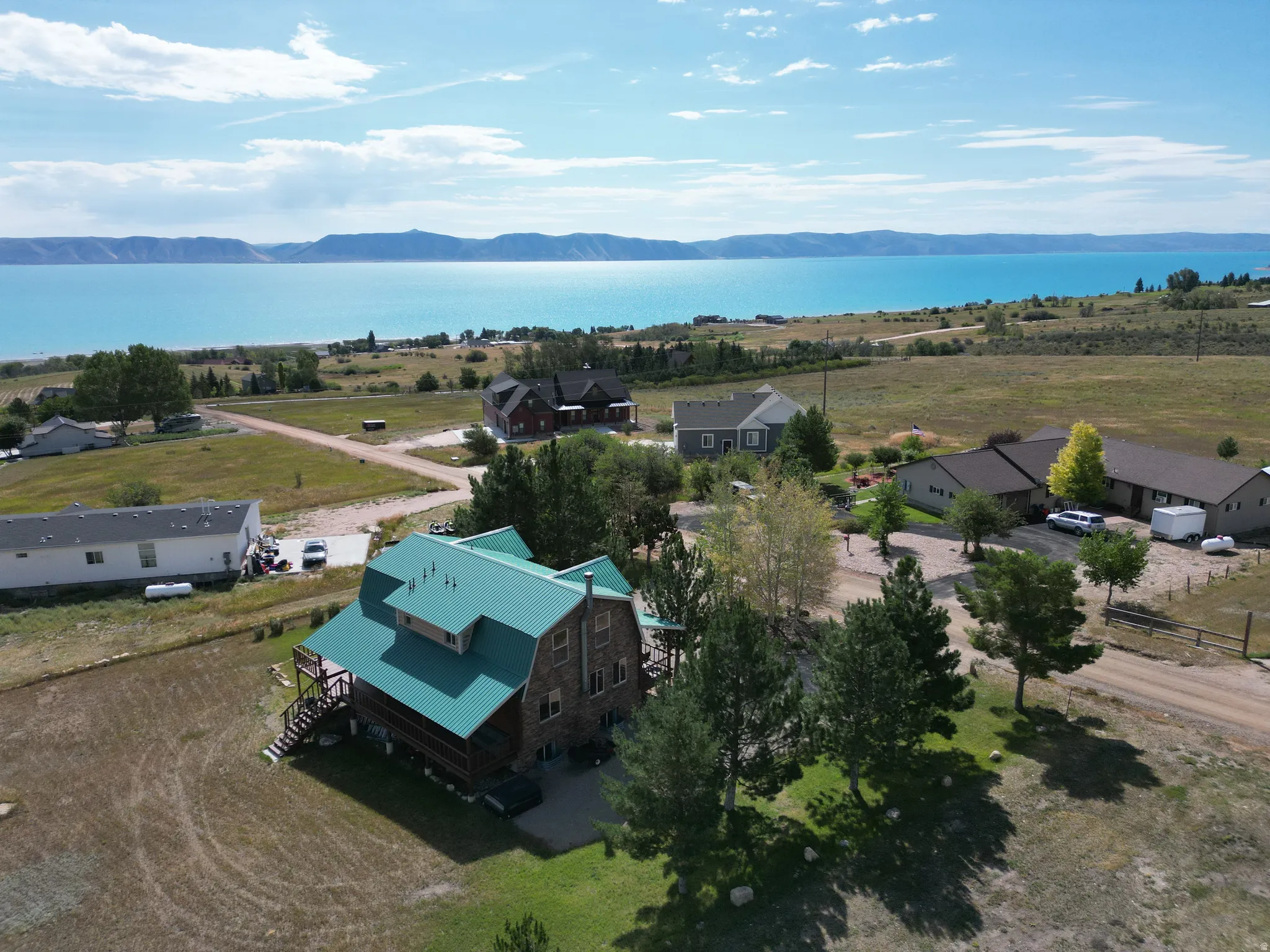 Wood-clad exterior with a green metal roof, multiple levels of outdoor decking, and a surrounding natural landscape