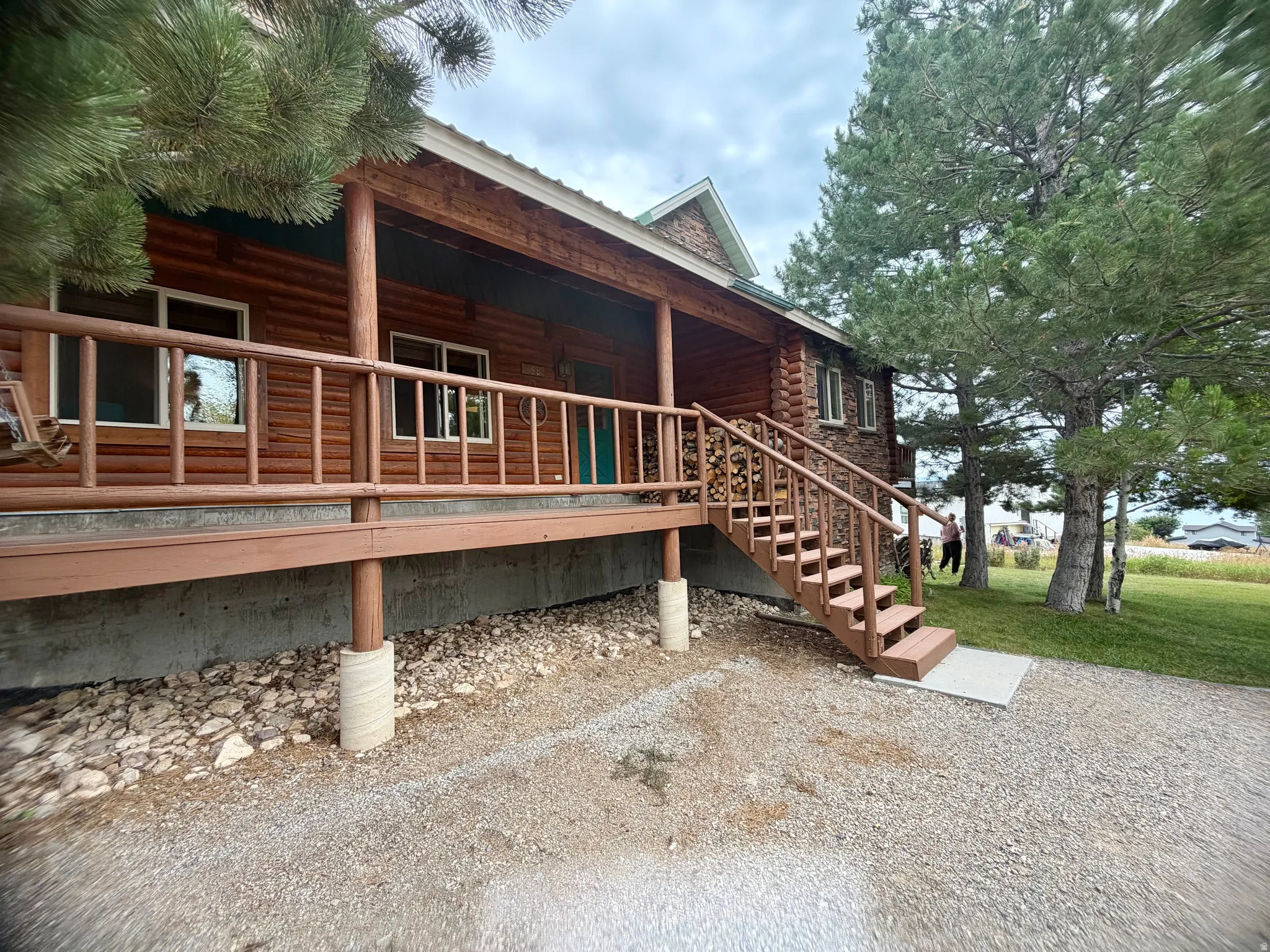 Log cabin exterior featuring a covered porch with wooden railings, a multi-level staircase, and a metal roof