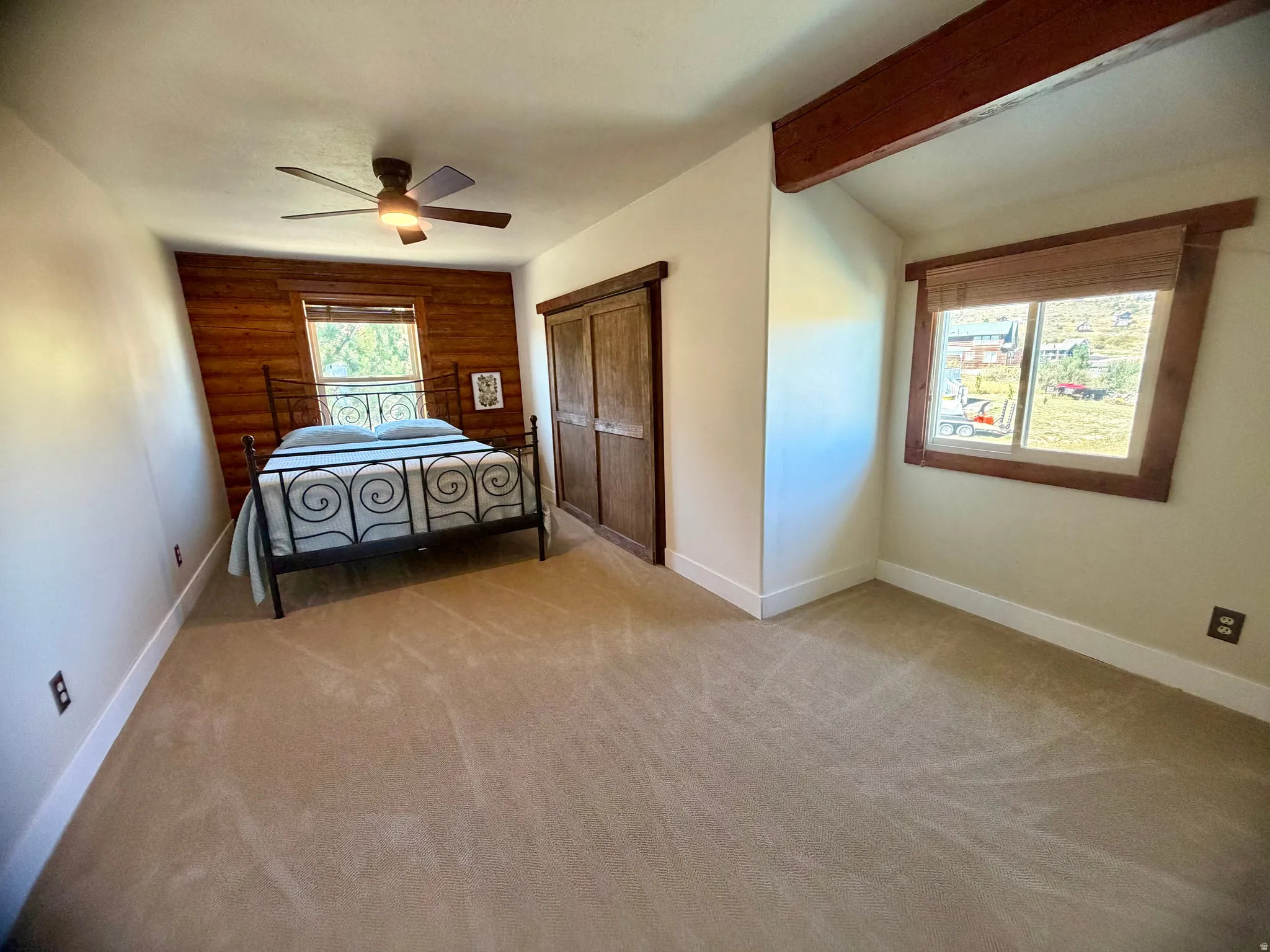 Carpeted interior with wood-paneled accent wall, exposed wood beam, and wooden window trim