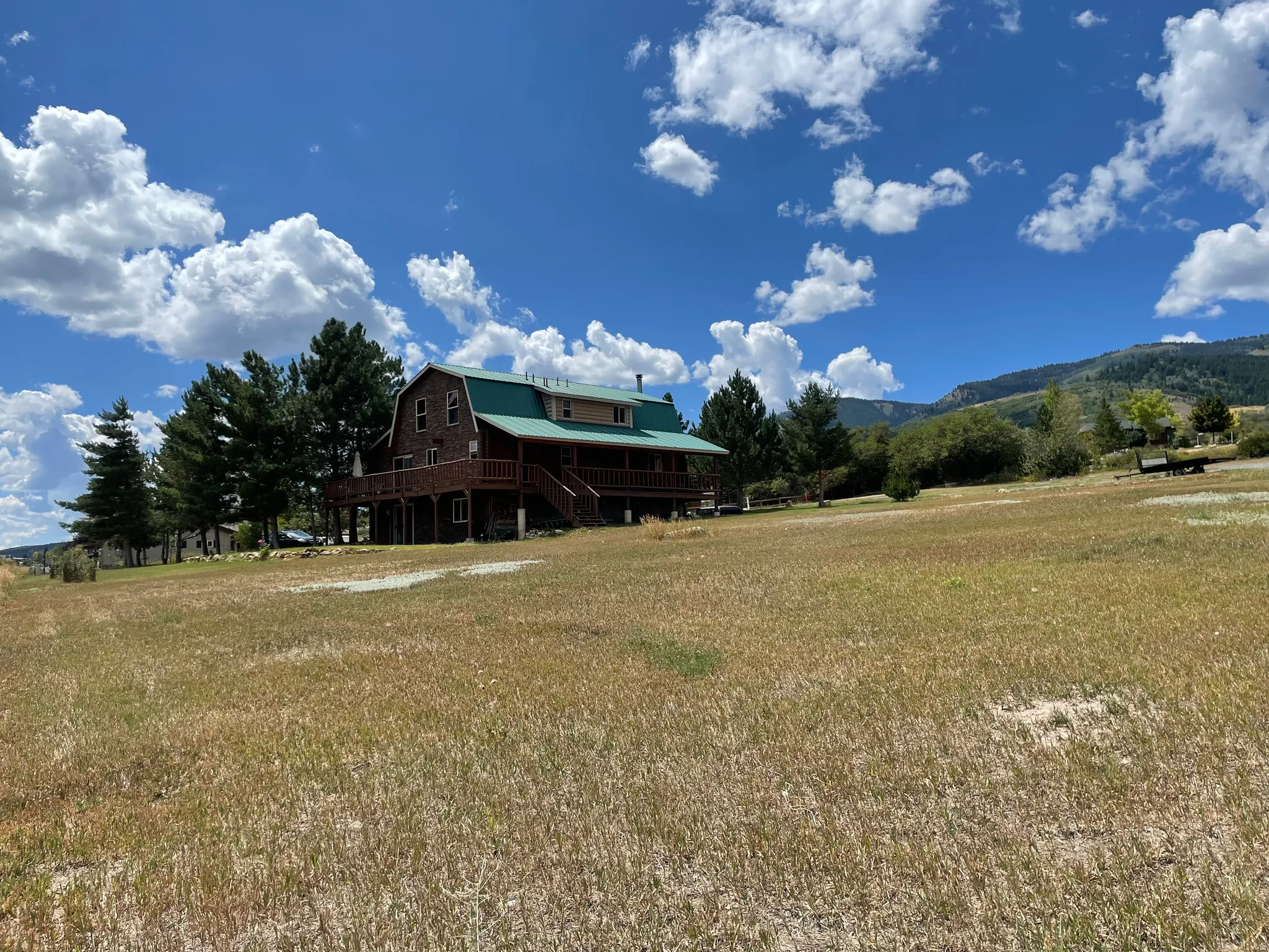 Two-story cabin-style residence with a green metal roof and an expansive wood deck