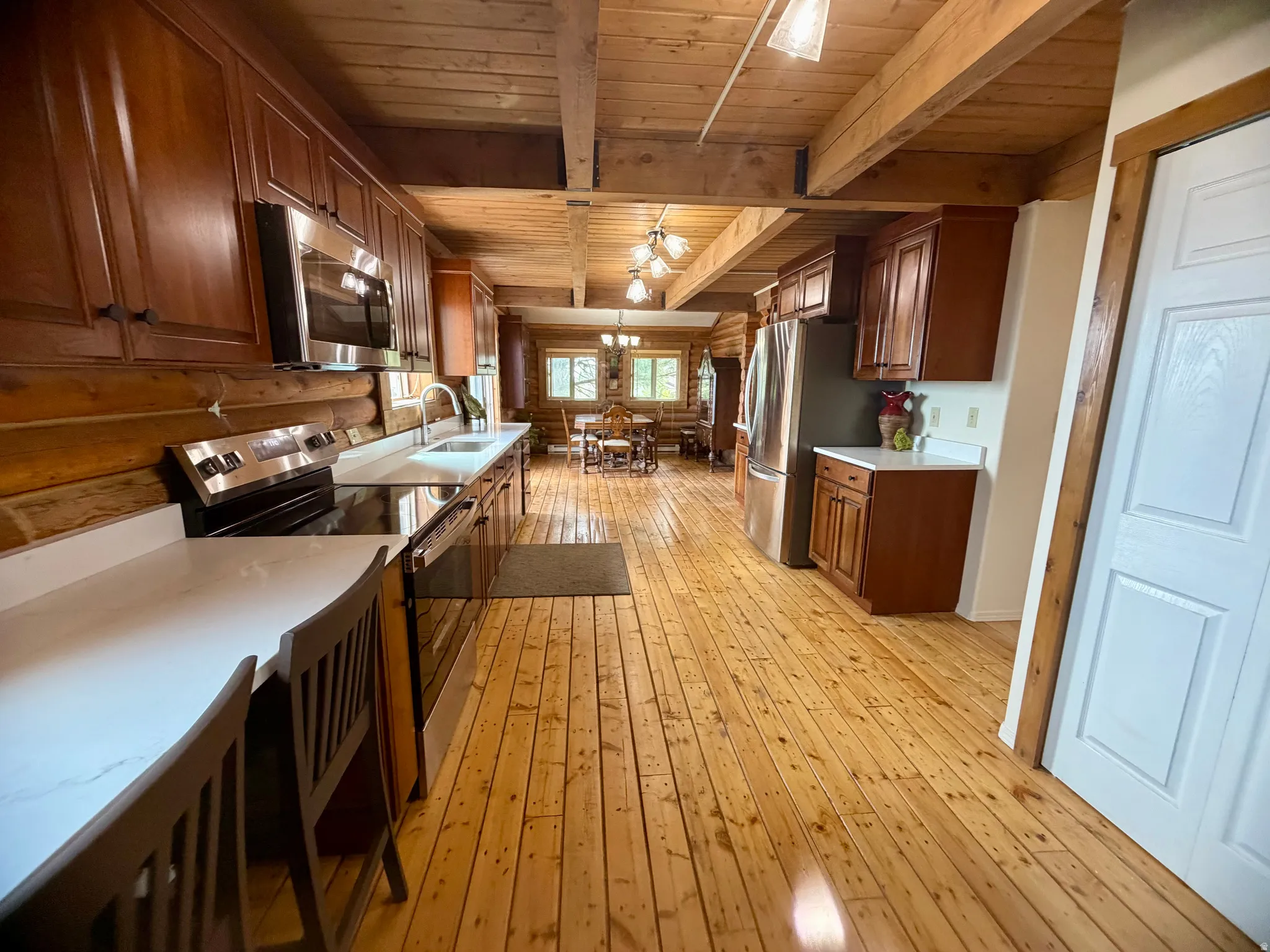 Kitchen with wood-finish flooring, exposed wood beam ceiling, stainless steel appliances, solid surface countertops, and wood cabinetry