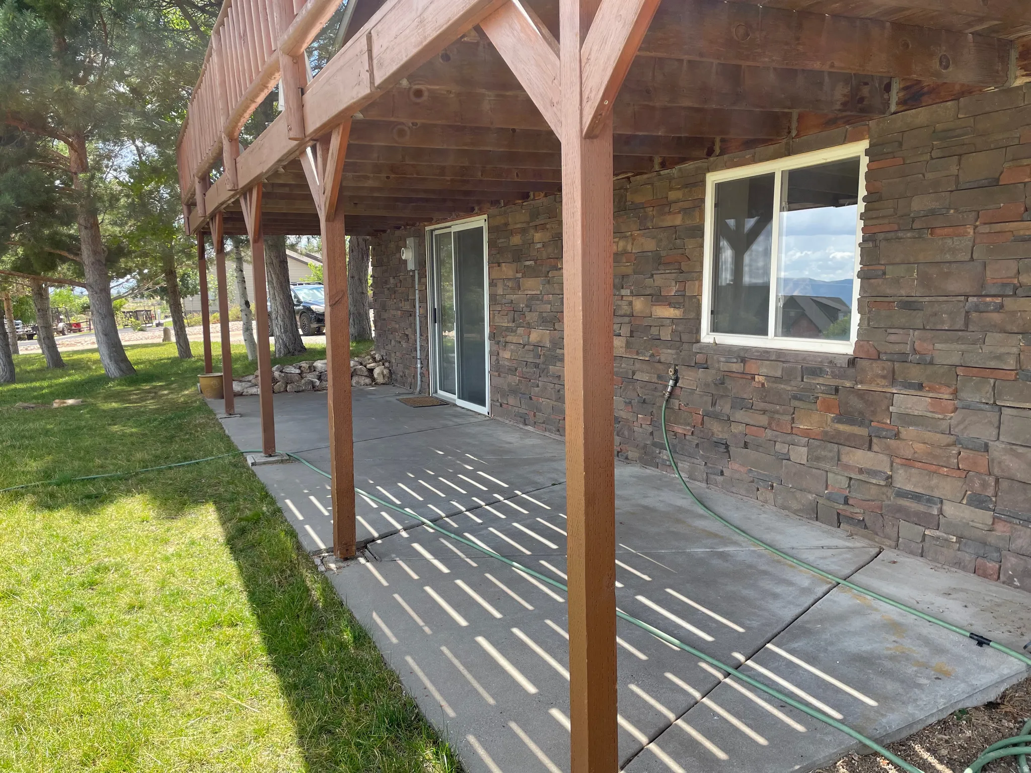 Stone veneer exterior with a ground-level patio, wood deck above, and sliding glass door access