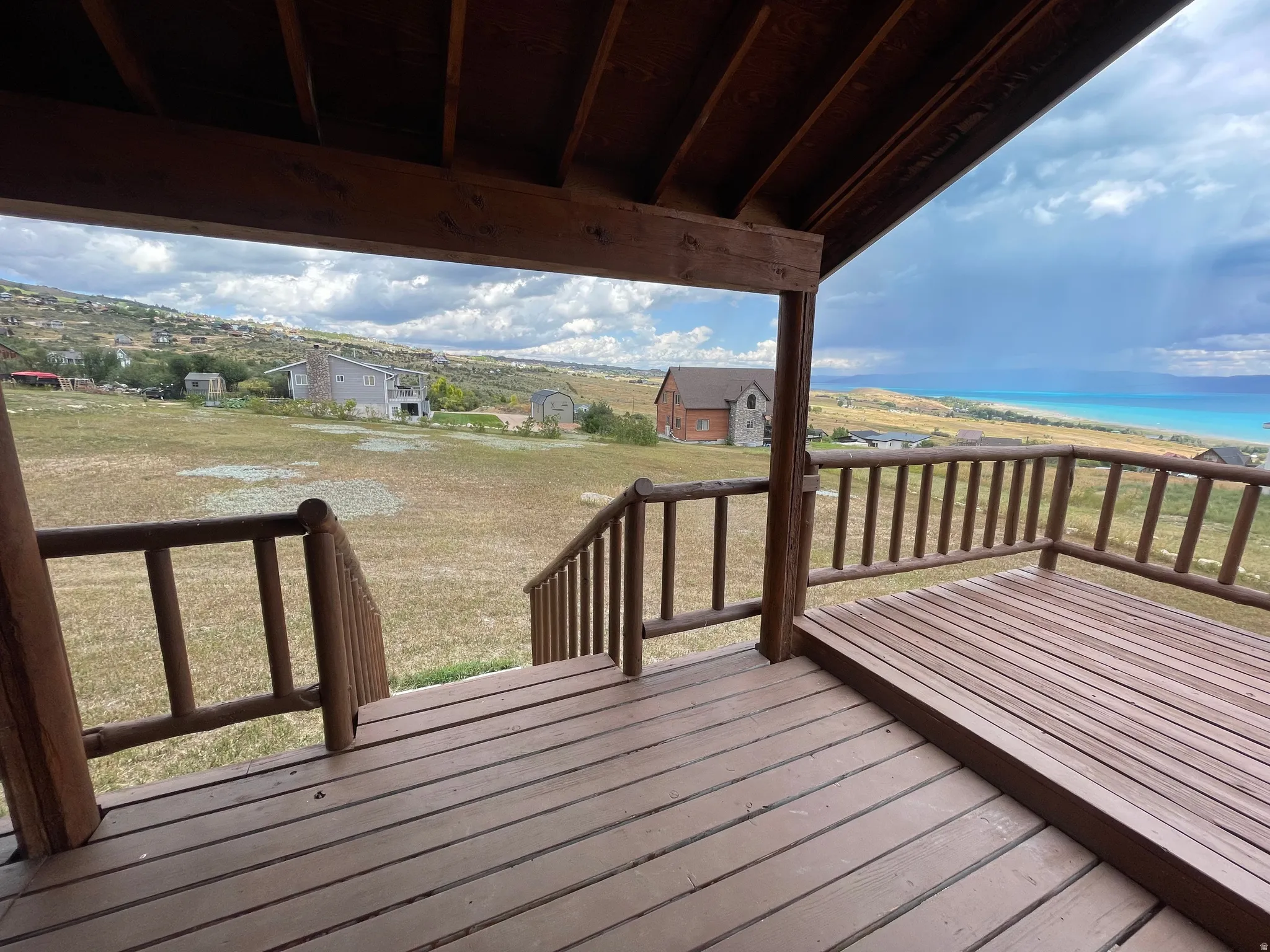Wood-finish deck with a rustic wooden railing, offering expansive landscape scenery and a distant body of water