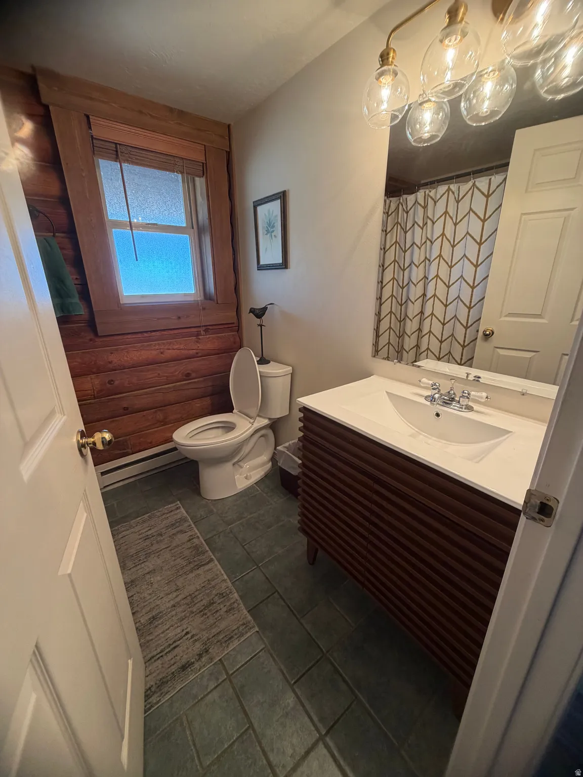 Bathroom featuring a wood-panel accent wall, square-tiled flooring, and a vanity with a white countertop and integrated sink