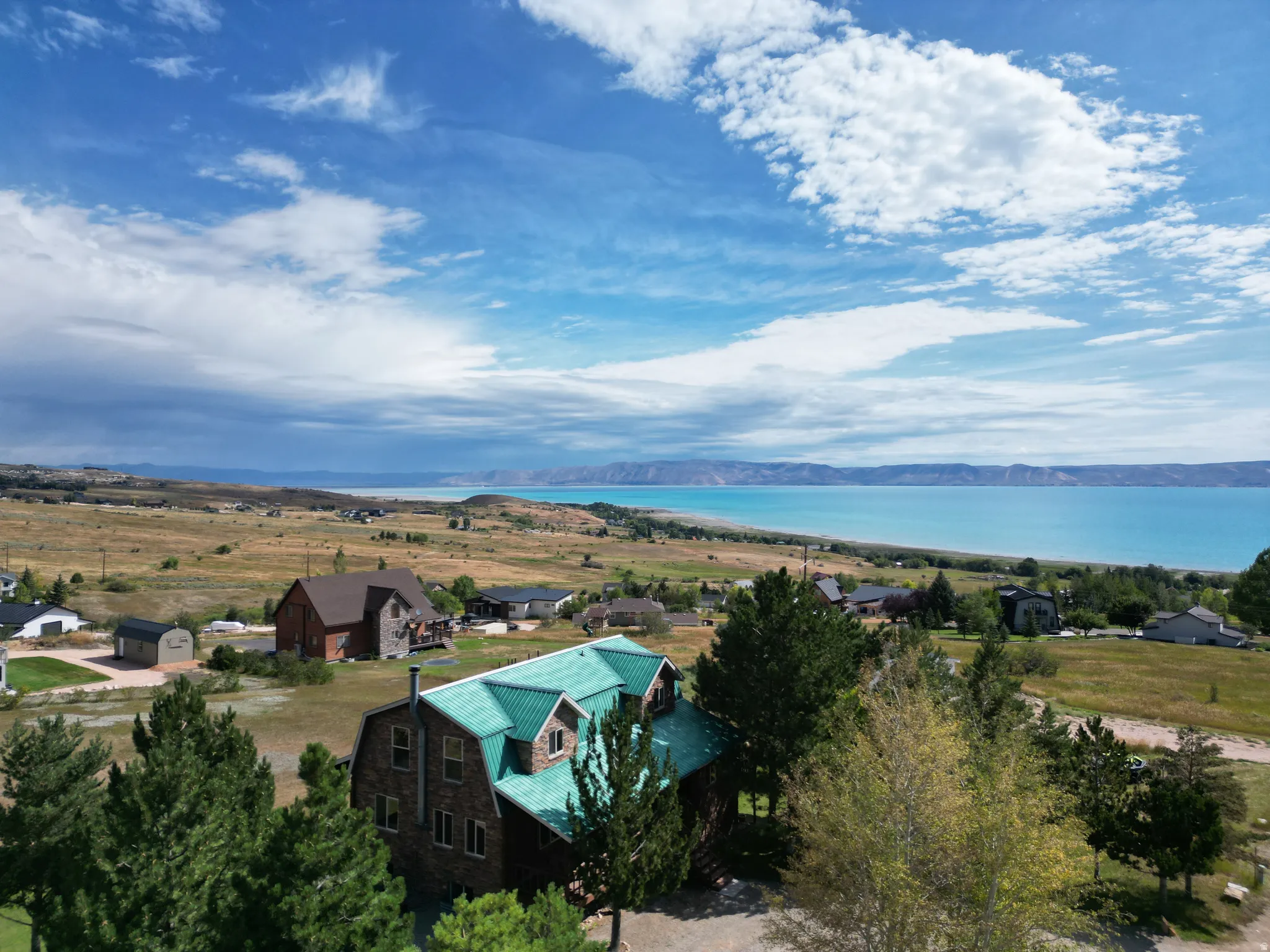 Property featuring a multi-level structure with a green metal roof, stone exterior, and surrounding natural landscape with distant water and mountain backdrops