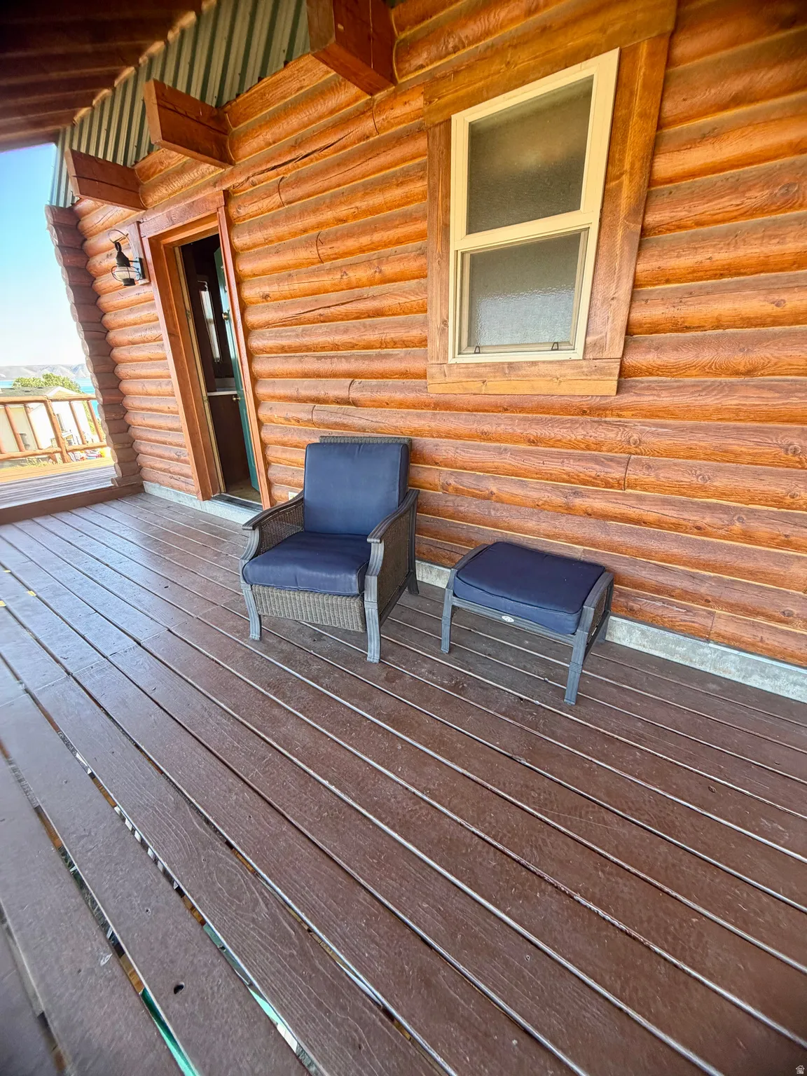 Covered exterior porch featuring log siding, composite decking, and a wall-mounted light fixture
