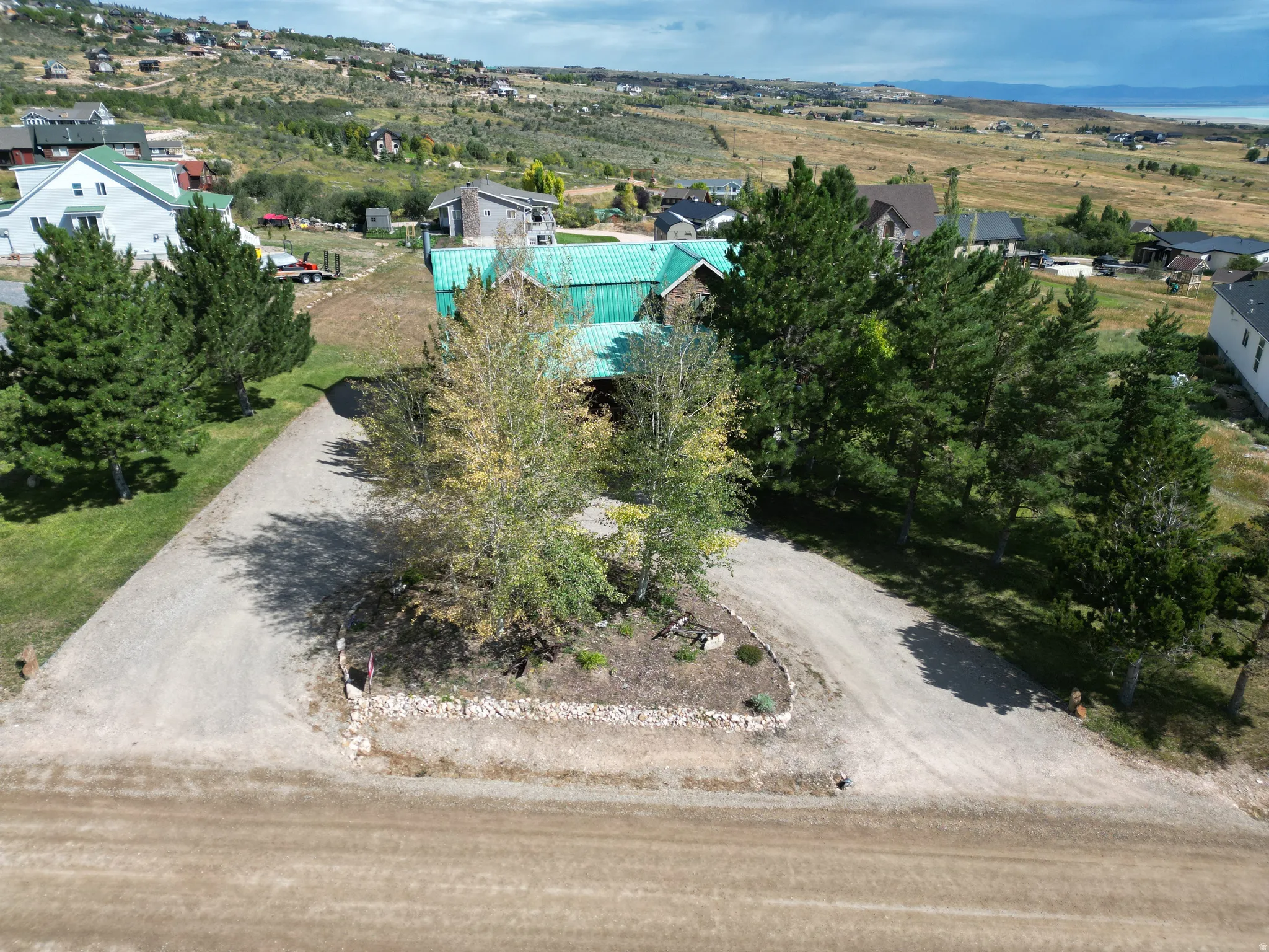 Gravel driveway with a central landscaped island, surrounded by mature trees and a copper-colored roof